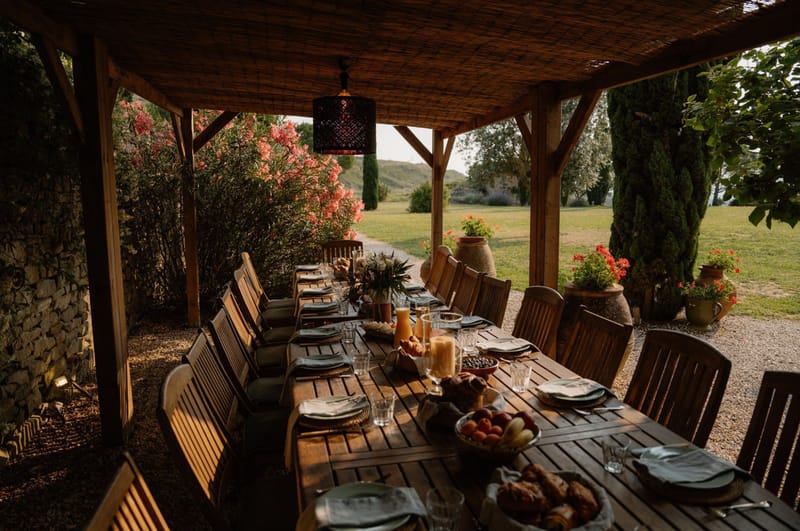 Wooden pergola with reed roof and pendant light over teak table set with sage napkins rattan placemats and stone fruit