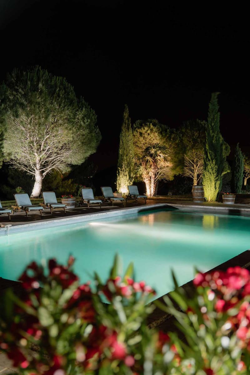 Illuminated turquoise swimming pool at night surrounded by cypress and palm trees in Provence