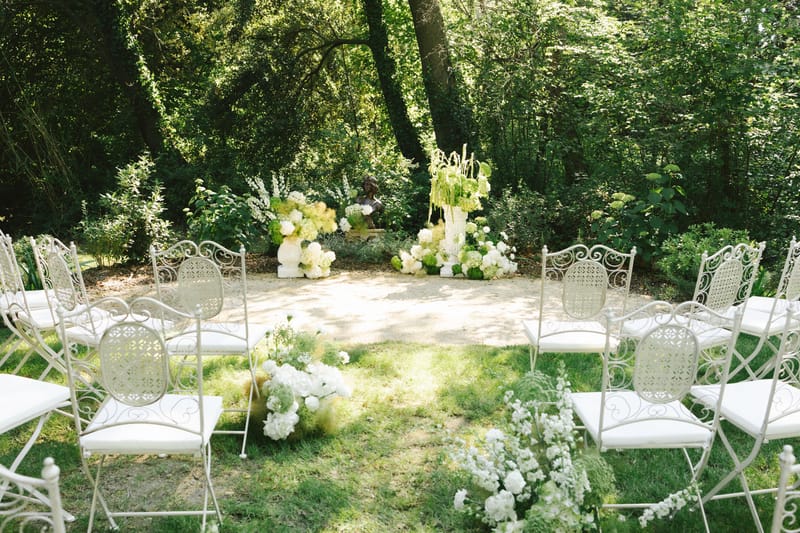 Ceremony setup with wrought-iron chairs and white hydrangea pedestals flanking bronze sculpture