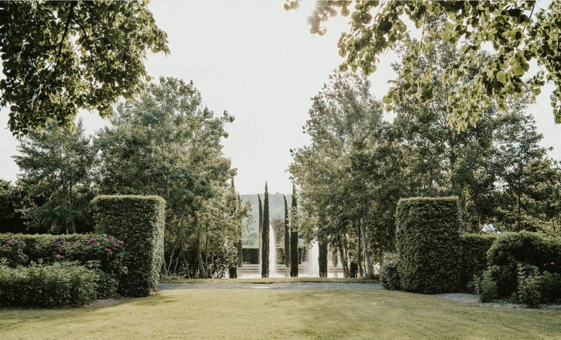 Formal French garden with symmetrical box hedges, gravel pathway, water fountain, and cypress trees