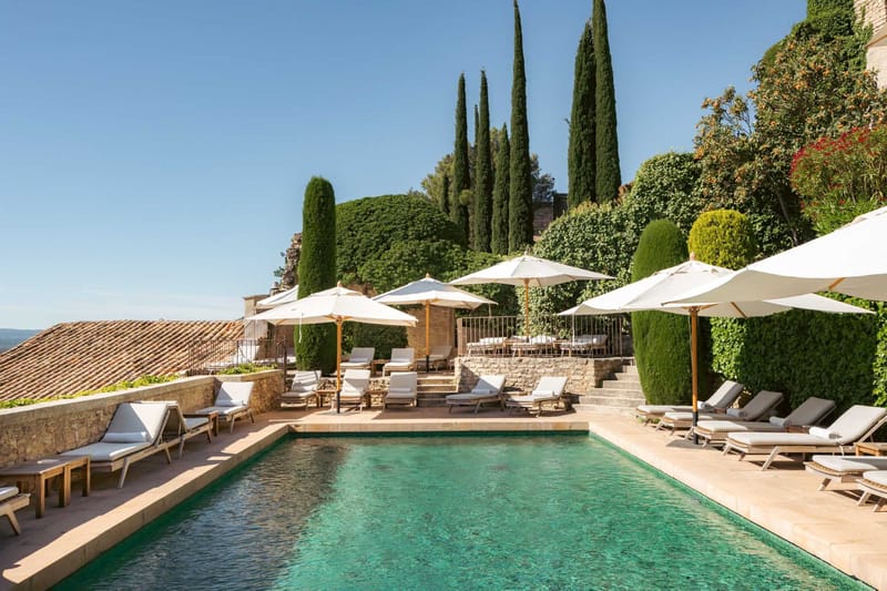Provencal stone-walled pool terrace with teak loungers, off-white umbrellas, and open countryside view