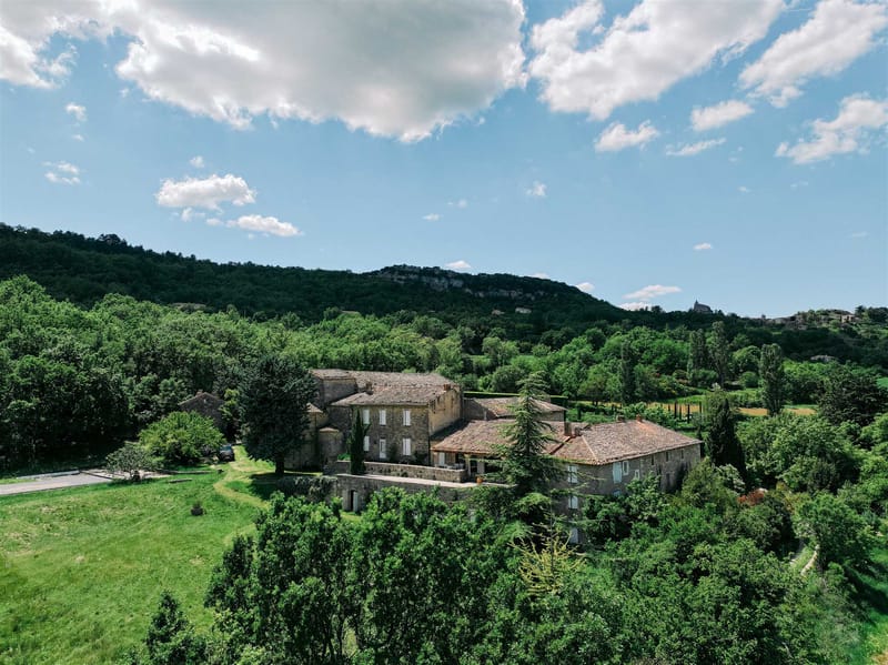 Aerial wide shot of stone estate with terracotta roofs surrounded by cypress trees and rolling countryside