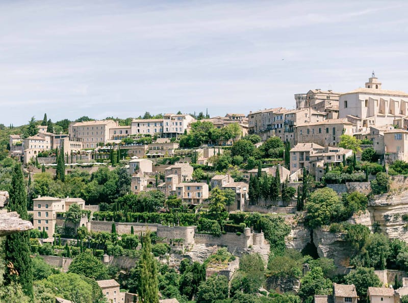 Medieval hilltop village in Provence with terracotta stone buildings, bell tower, cypress trees and river below