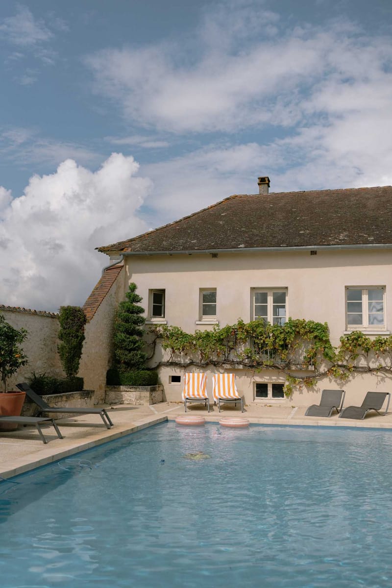 French country house with swimming pool, striped sun loungers, topiary shrubs, and climbing vines on facade