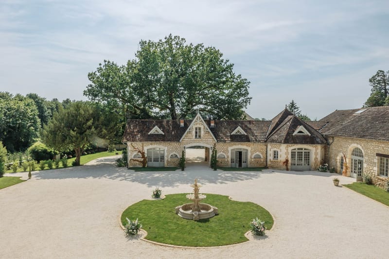 Aerial view of limestone outbuilding with arched gateway, circular fountain, and gravel forecourt