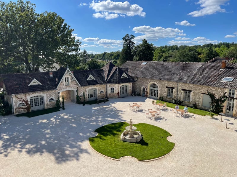 Aerial view of U-shaped French limestone estate with gravel courtyard, stone fountain, and topiary entrance
