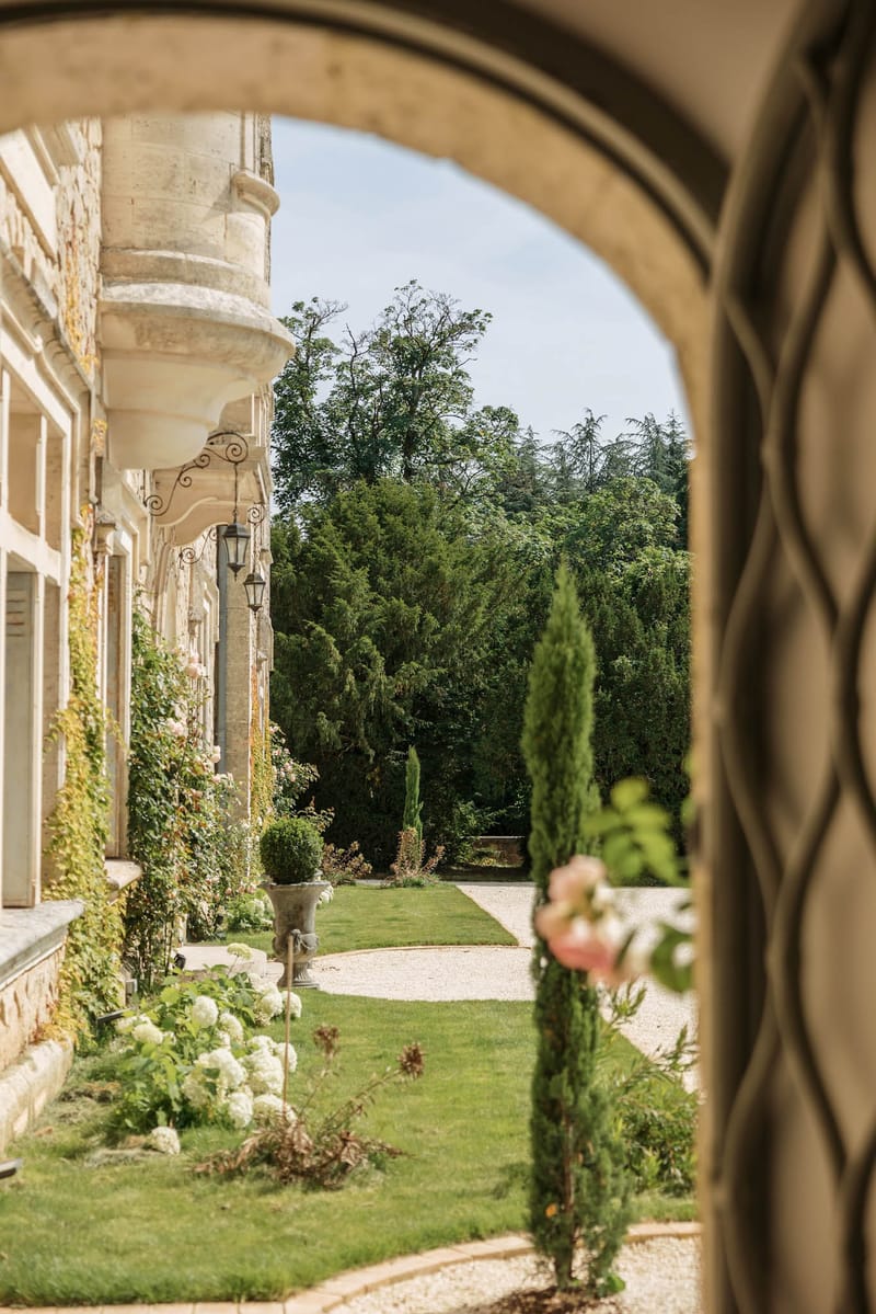 Chateau de la Couronne exterior viewed through arched doorway with formal garden, topiary, and hydrangeas