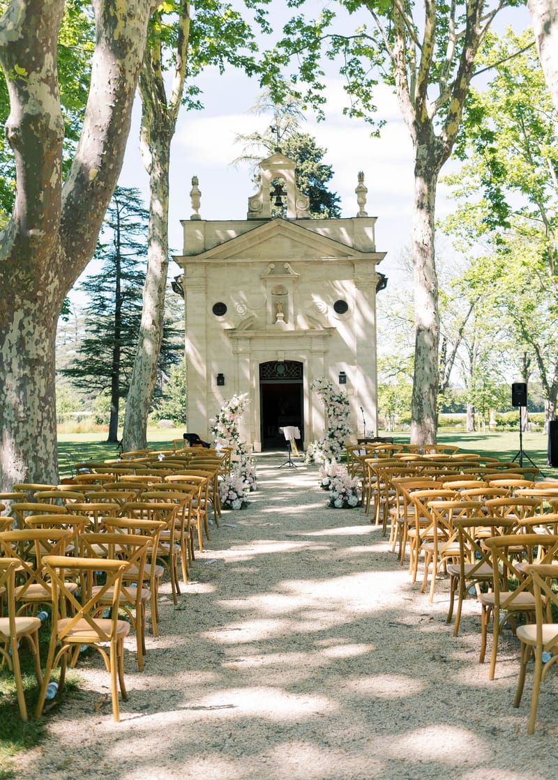 Ceremony setup with cross-back chairs facing stone chapel entrance flanked by white and blush arrangements
