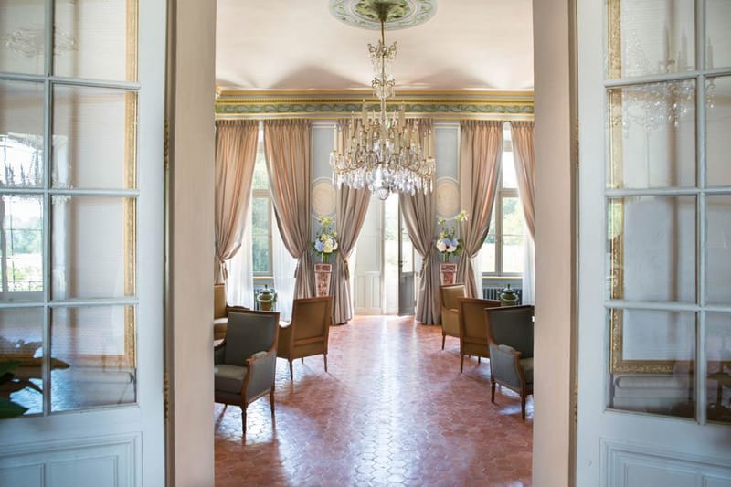 Chateau salon with crystal chandelier, blush silk curtains, period armchairs, and painted ceiling frieze