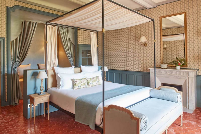 Chateau guest suite with black four-poster canopy bed, blue wood paneling, white marble fireplace, and terracotta tile floor