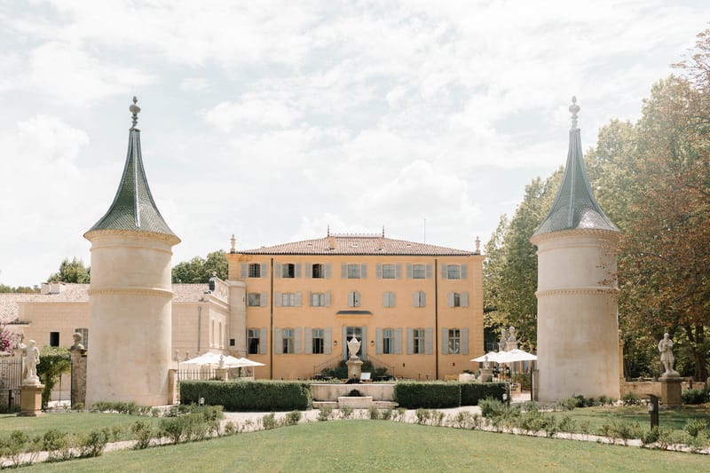 Ochre-yellow chateau with stone gatehouse towers, parterre garden, and central fountain from lawn approach
