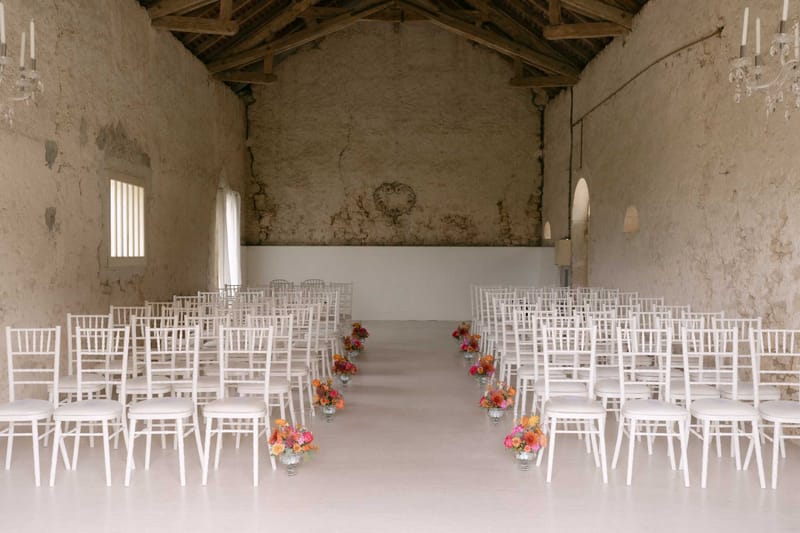 Rustic barn ceremony setup with white chiavari chairs and orange and pink floral aisle arrangements