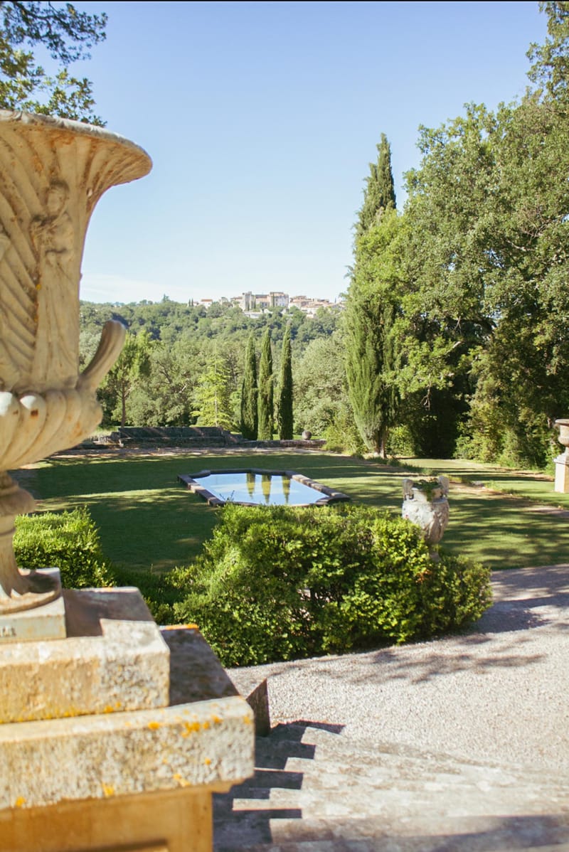 Stone terrace view over formal French gardens with boxwood hedging, mirror pool, and cypress trees