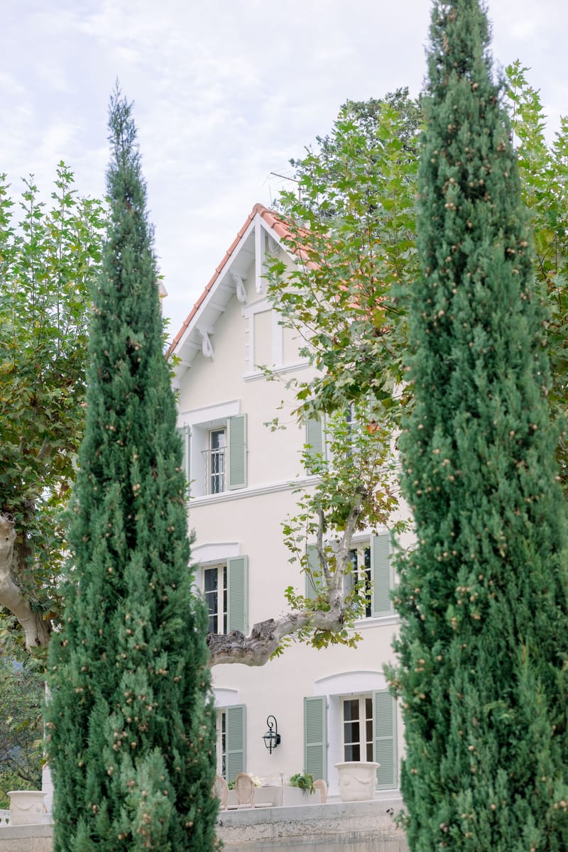 Three-storey cream villa with green shutters framed symmetrically by tall cypress trees at European estate