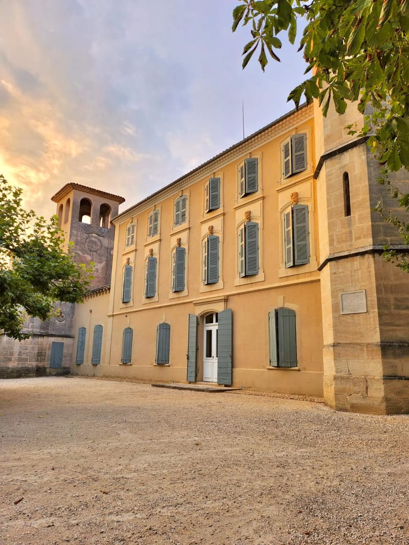 Three-storey ochre Provencal manor with slate-blue shutters, stone bell tower, and gravel courtyard