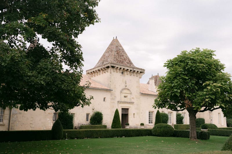 French chateau with round tower, conical terracotta roof, formal parterre hedging, and manicured lawn