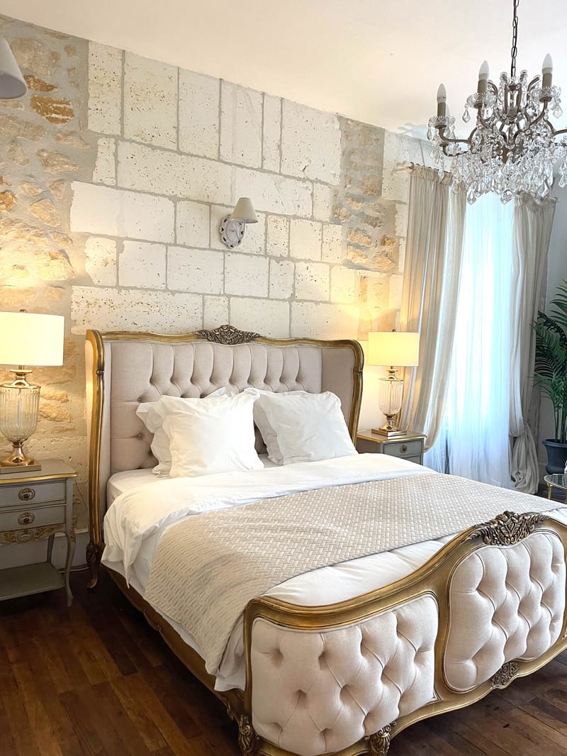 Louis XV bed with gold frame and crystal chandelier in limestone-walled chateau guest bedroom