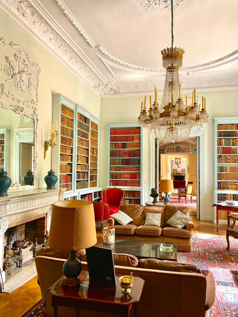 Grand chateau library with floor-to-ceiling pale blue bookshelves, crystal chandelier, and antique furnishings