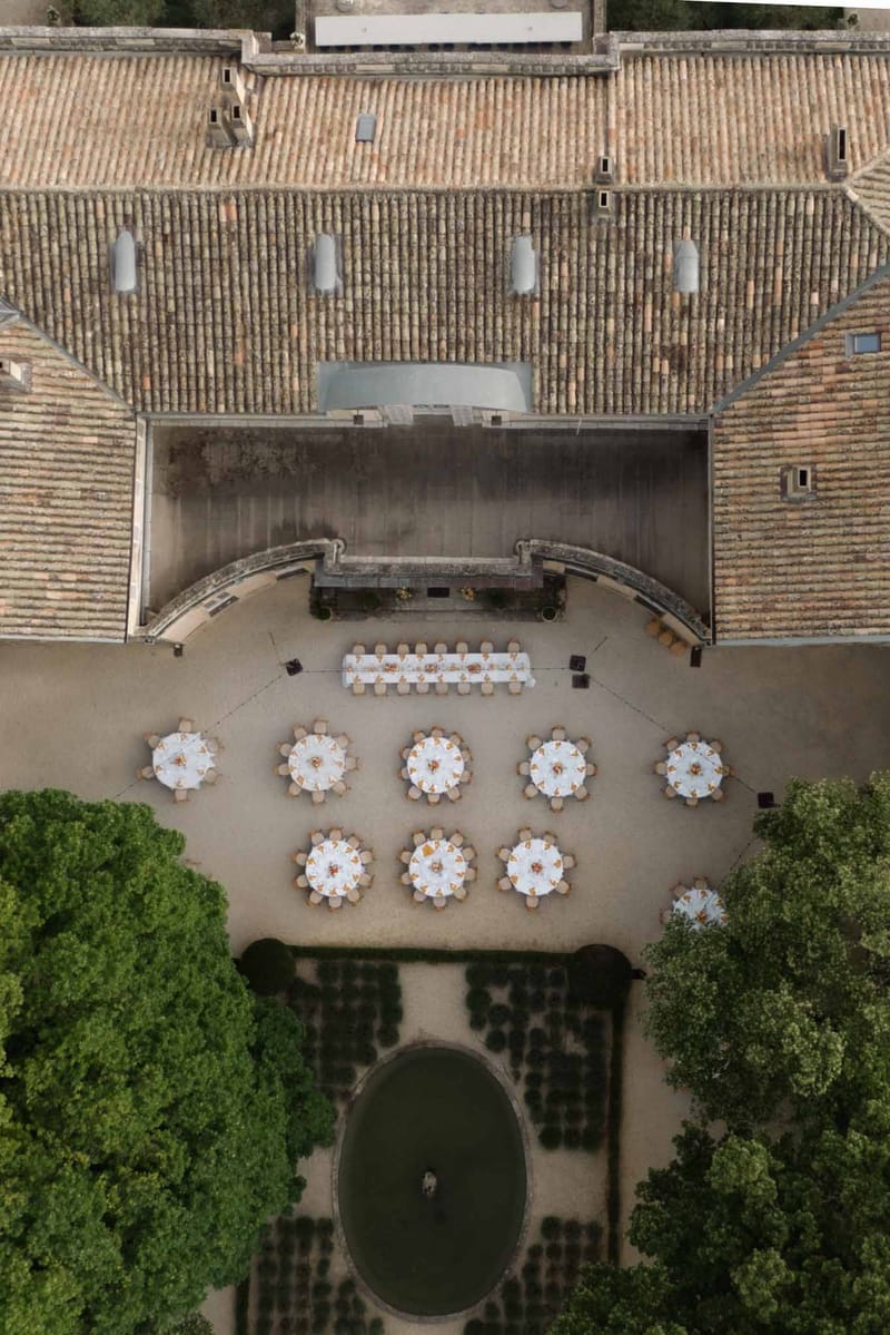 Aerial view of stone courtyard reception with white-linen round tables, terracotta tile roofs and manicured hedges