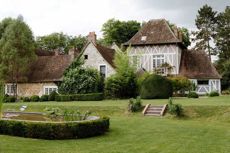 Historic Norman manor house with half-timbered facade, rectangular pond, manicured lawns and topiary on expansive grounds