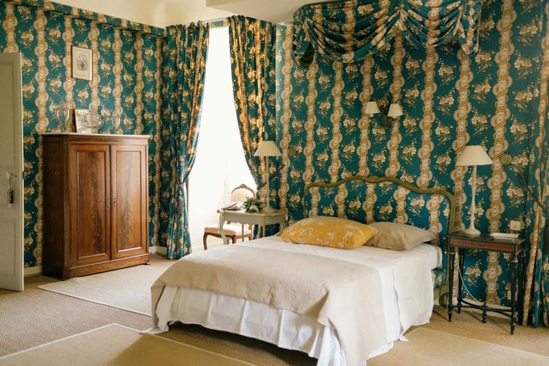 Chateau guest bedroom with teal and gold floral wall fabric, canopy bed, and antique walnut armoire