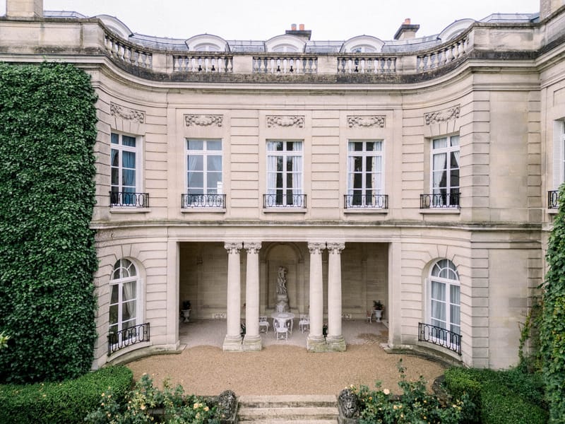 Neoclassical French mansion facade with Ionic columns, wrought-iron balconies, and gravel forecourt