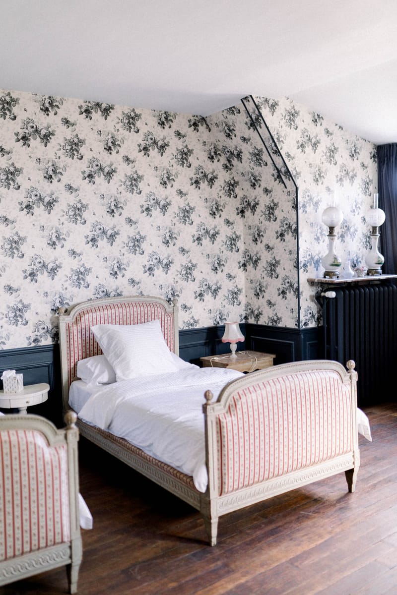 Classic French chateau bedroom with Louis XVI bed, rose-patterned wallpaper, navy wainscoting, and period furnishings