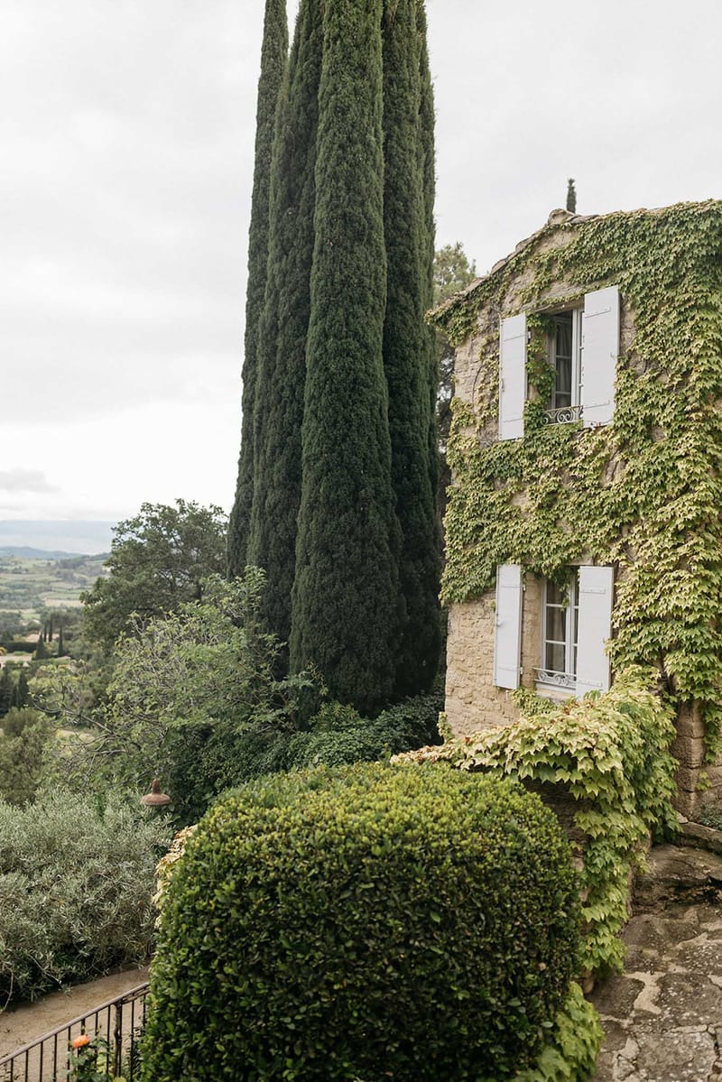 Stone villa with ivy-covered walls and cypress tree on hillside with panoramic Tuscan landscape views