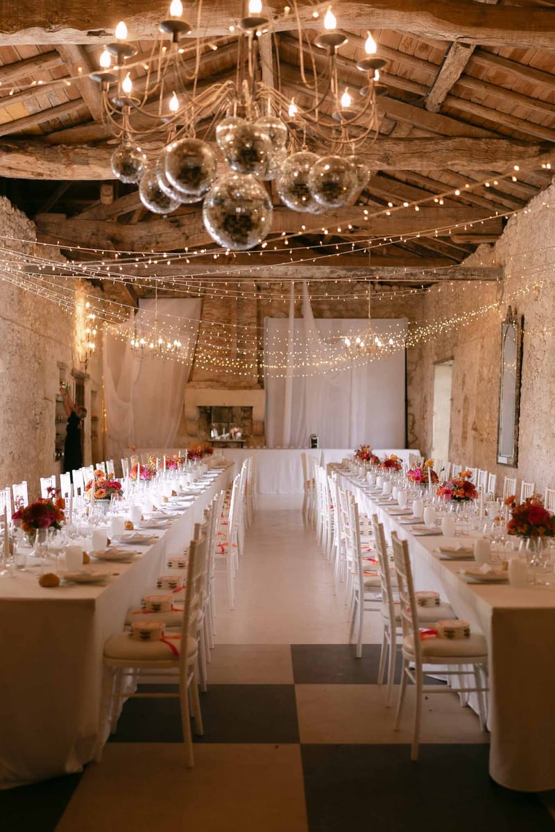 Rustic stone barn reception with long banquet tables, fairy lights, disco balls, and fuchsia and orange floral centerpieces