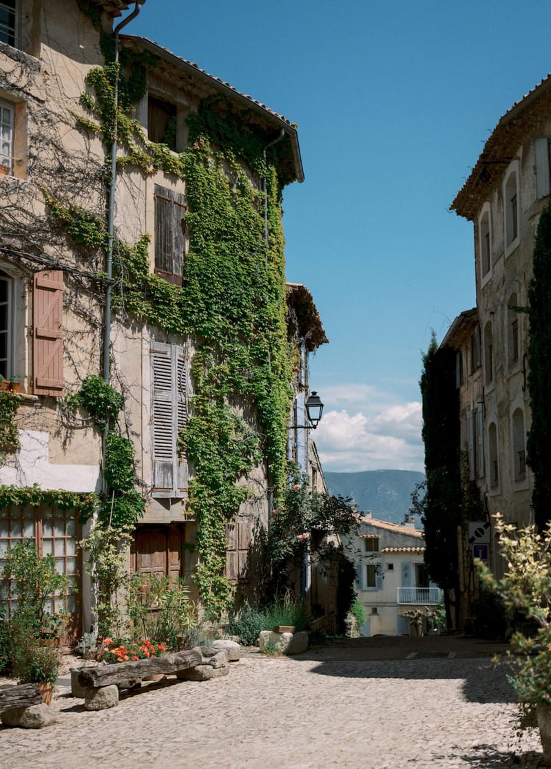 Cobblestone street in a Provencal village with stone buildings, wooden shutters, and distant mountain view