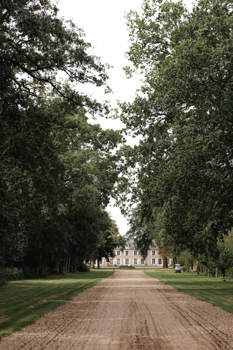 Tree-lined driveway leading to classical stone château wedding venue with manicured grounds
