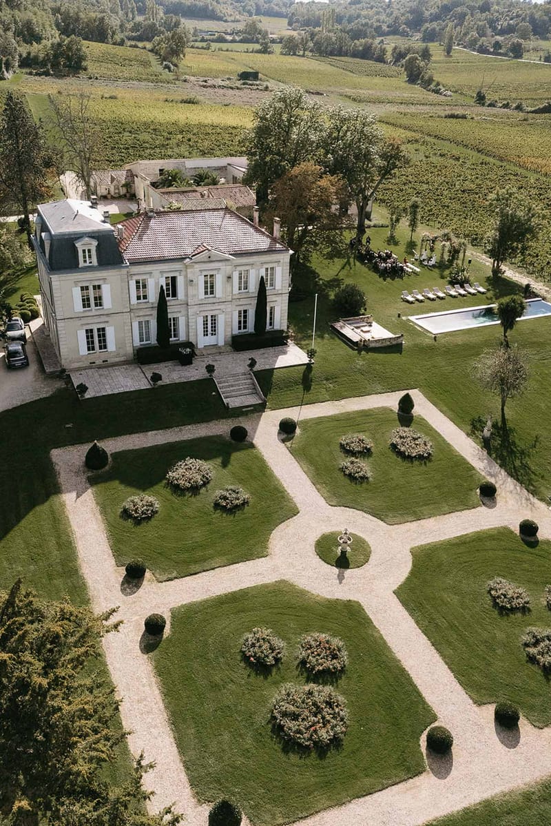 Aerial view of limestone chateau with parterre garden, swimming pool, and outdoor wedding ceremony on wine estate
