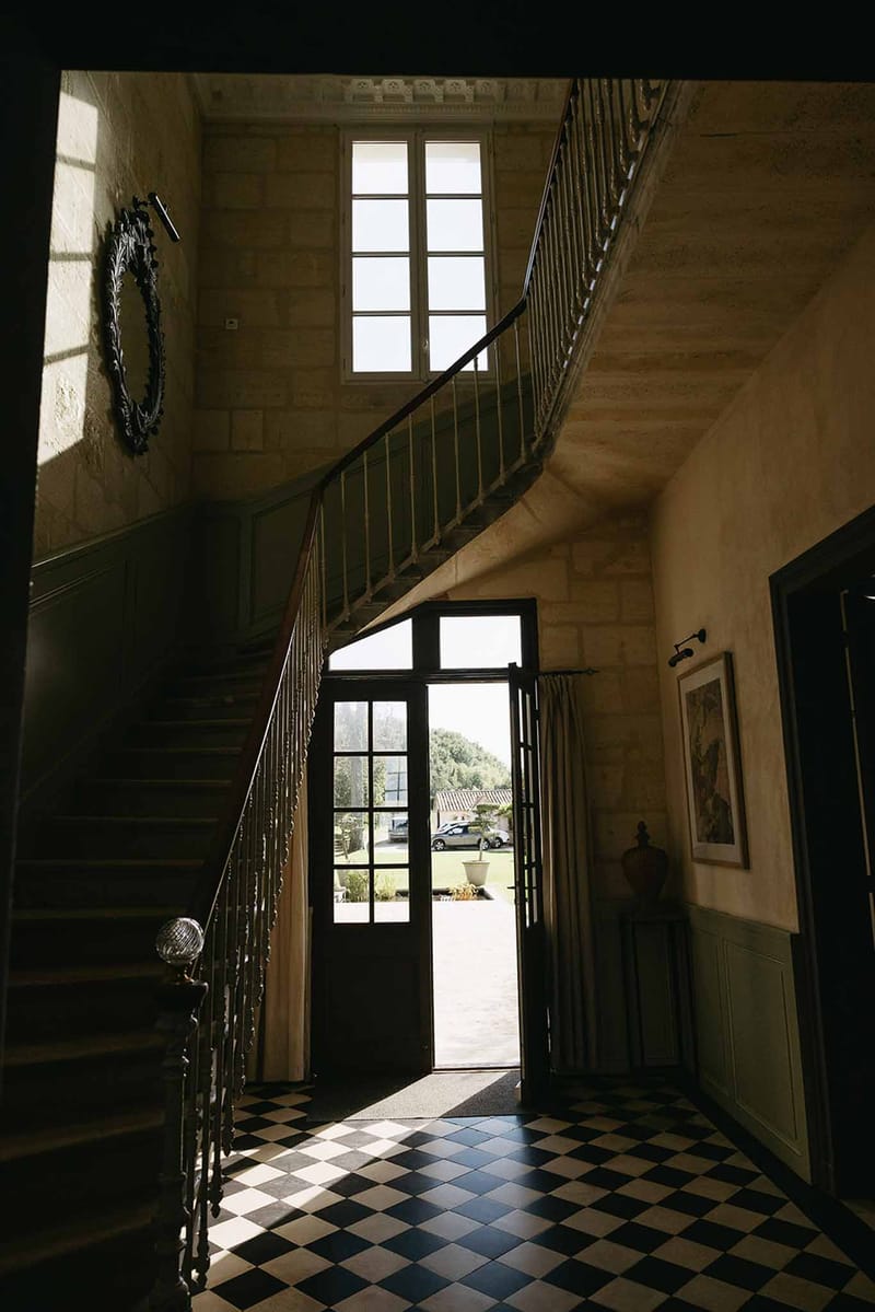 Grand chateau entrance hall with black and white tiled floor, curved staircase, wrought-iron balustrades, and tall windows