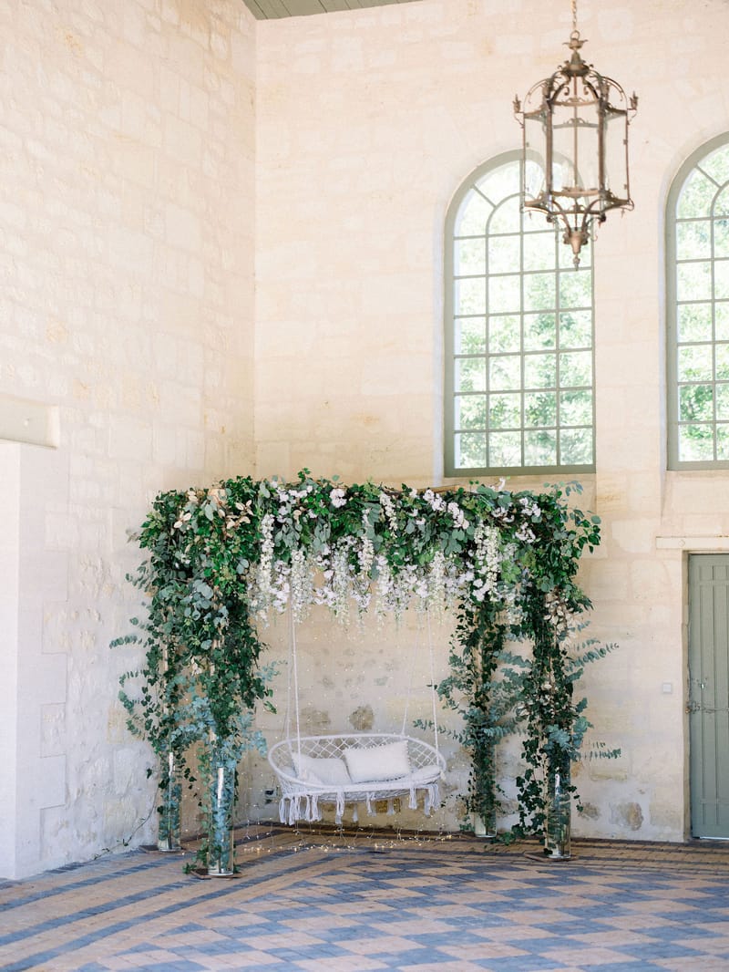Macrame swing on greenery arch with fairy lights in limestone room with geometric tiled floor