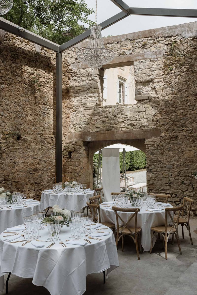 Reception setup in historic stone courtyard with round tables and crystal chandelier