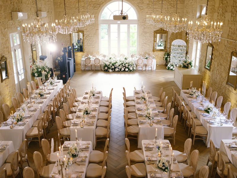 Overhead view of chateau ballroom reception with banquet tables, white floral garlands and crystal chandeliers