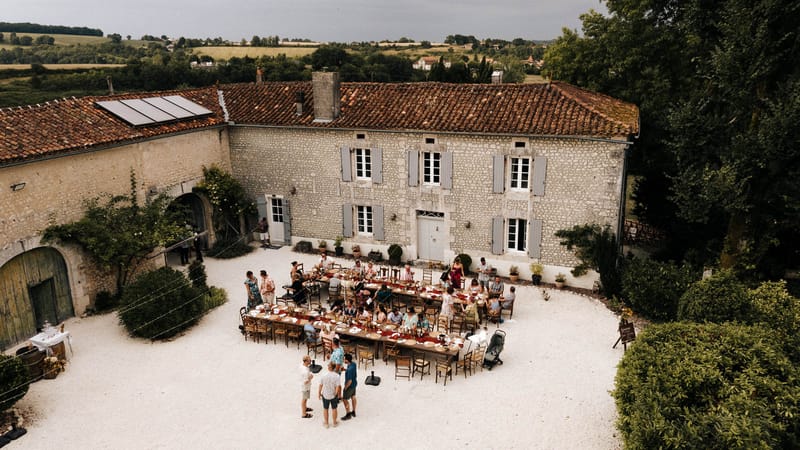 Aerial courtyard reception at stone farmhouse with burgundy runners, mismatched chairs, and fairy lights overhead