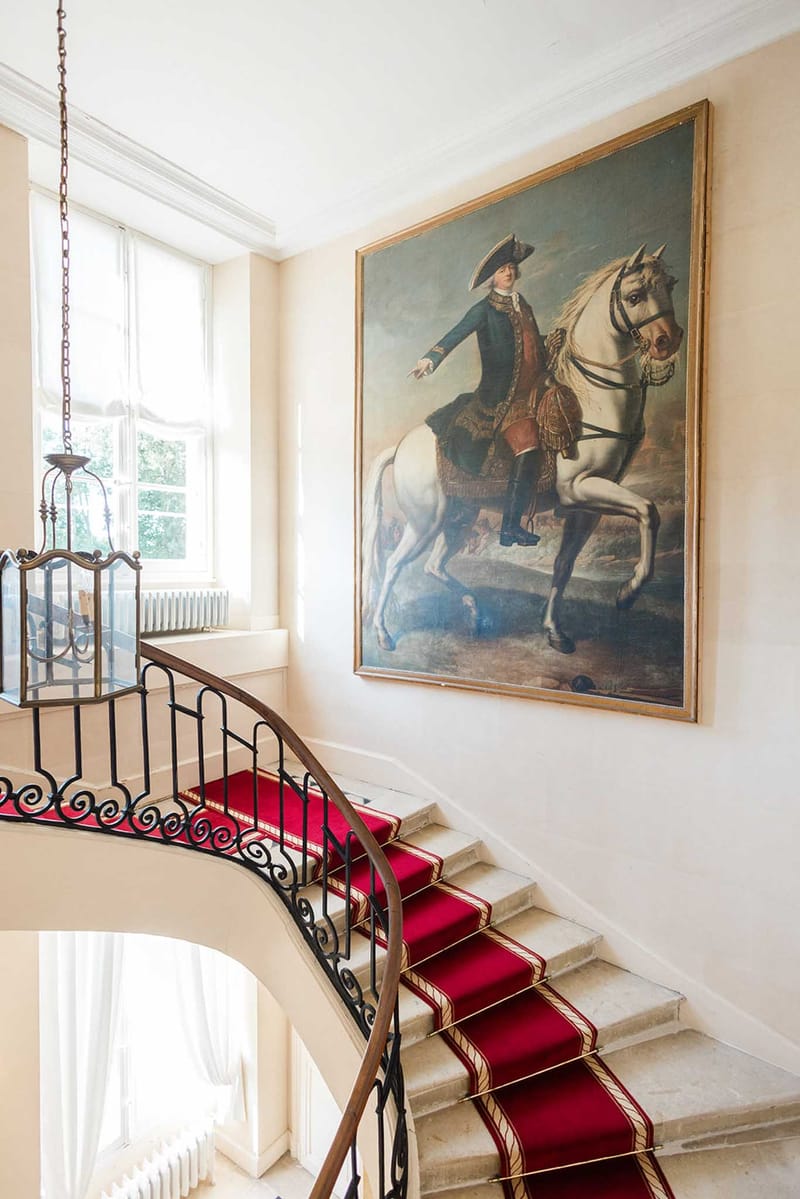 Grand chateau staircase with crimson carpet, wrought-iron balustrade and gilt-framed equestrian portrait painting