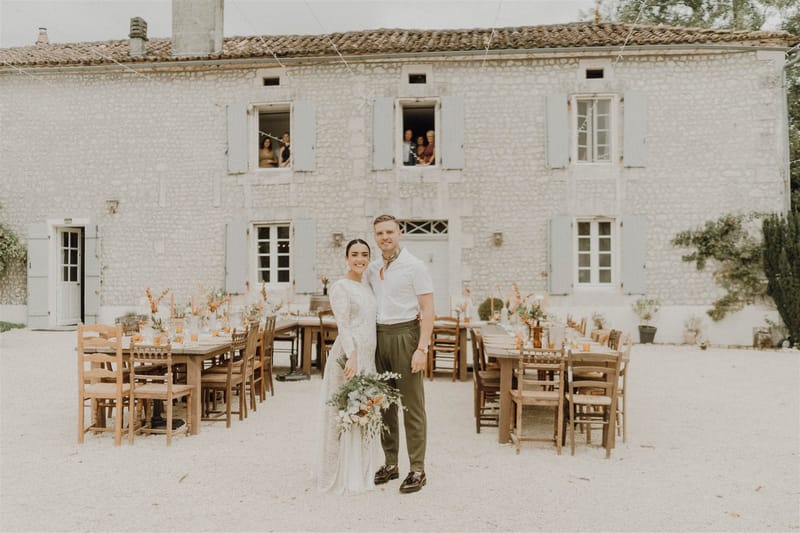 Couple at rustic farm table with amber glassware and terracotta florals before stone farmhouse