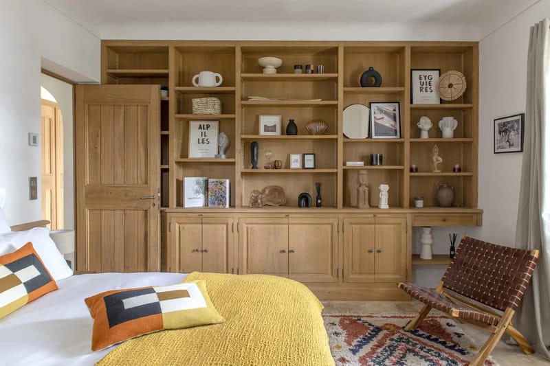 Modern Provencal guest bedroom with oak shelving, mustard coverlet, leather chair, and Berber rug