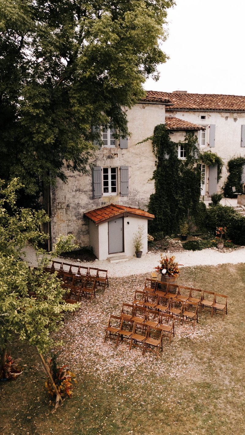 Aerial ceremony setup with pampas-topped barrel altar, rust floral aisle markers, and 30 chairs at stone manor