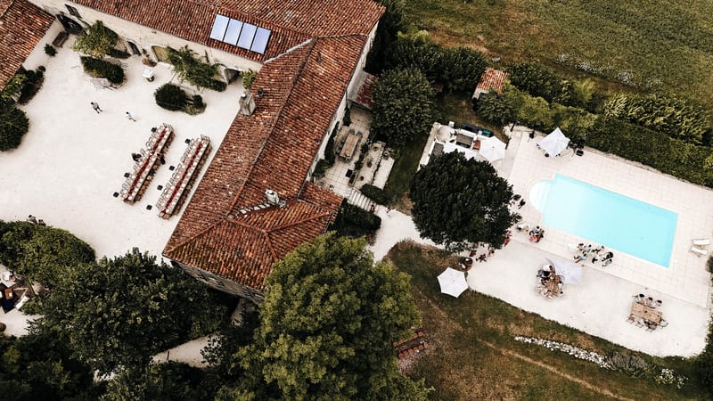 Aerial view of farmhouse venue with courtyard banquet tables pool with umbrellas and white canopy tent