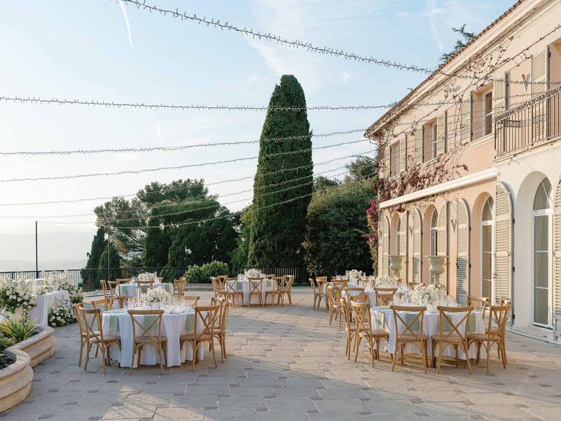 Reception terrace setup with round tables at classical French chateau with string lights and formal gardens