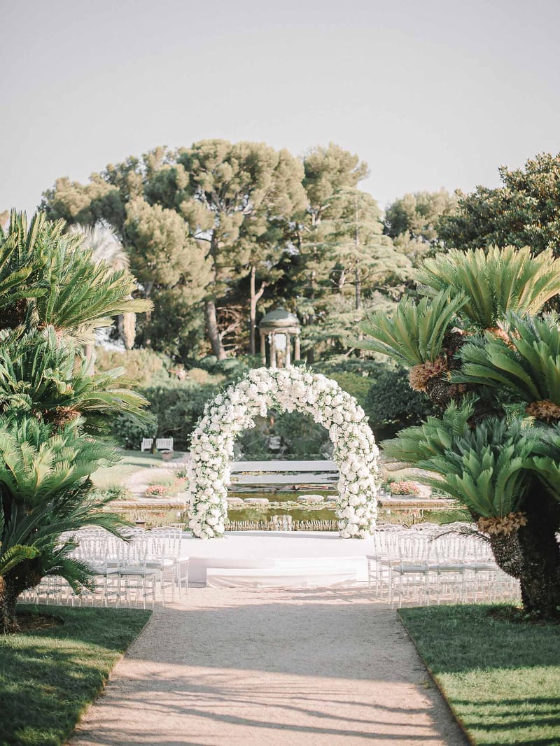 Mediterranean garden ceremony setup with white floral arch and chiavari chairs at historic venue terrace
