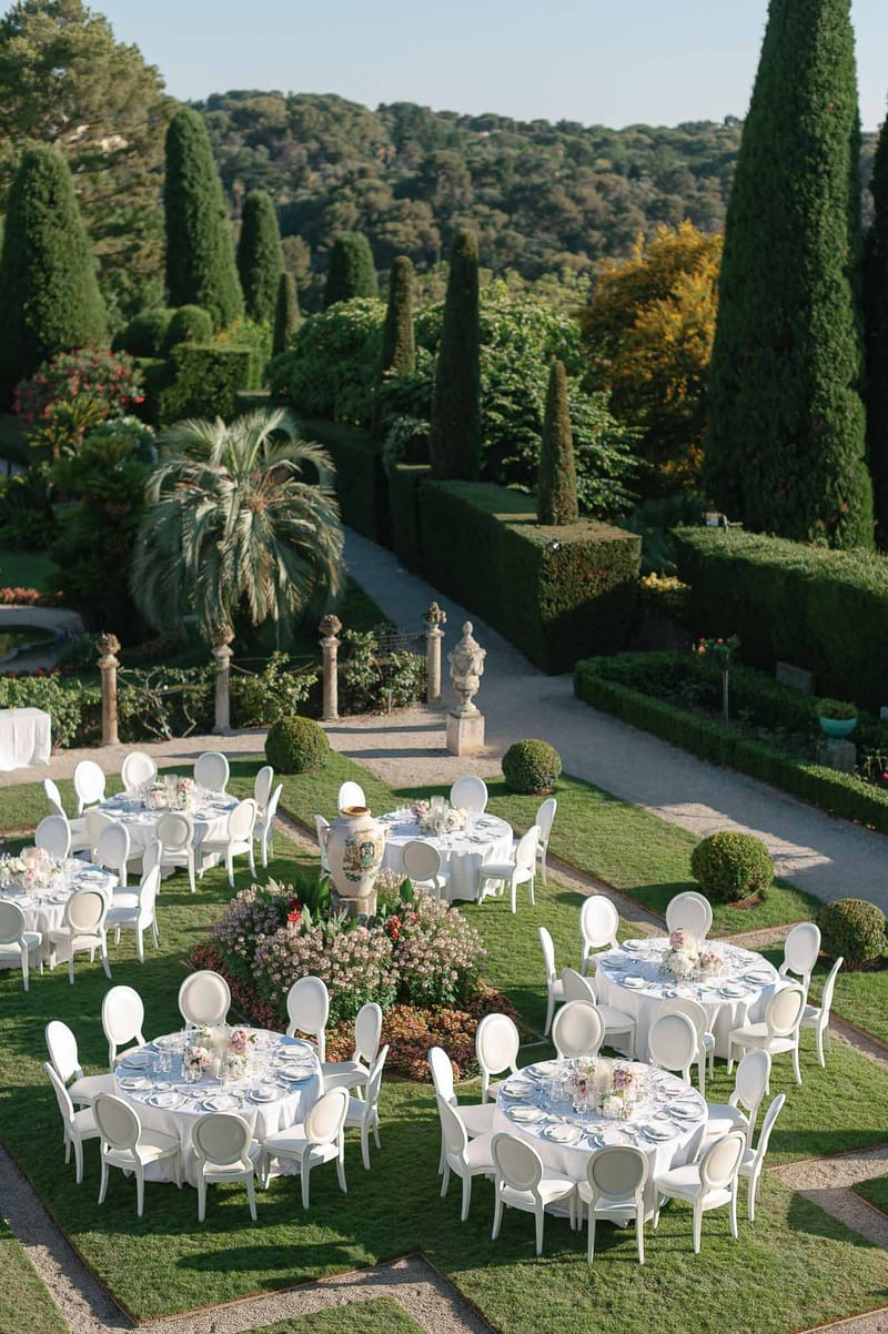 Outdoor wedding reception setup in Mediterranean garden with formal landscaping and cypress trees
