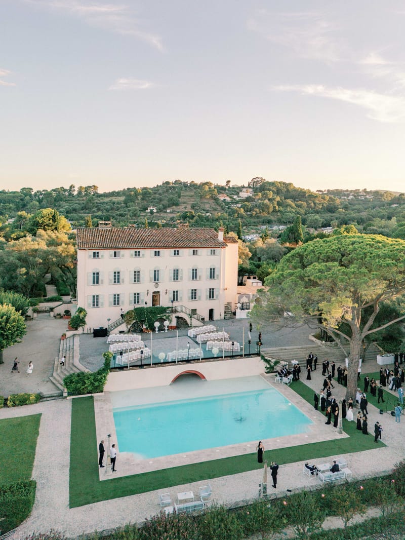Aerial view of cocktail hour by a pool at a Provencal bastide with guests mingling at golden hour
