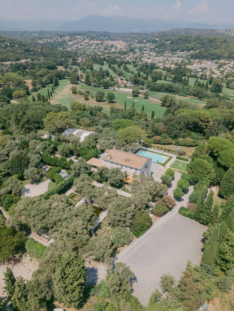 Aerial view of Provencal bastide estate with pool, formal gardens, golf course, and mountain backdrop