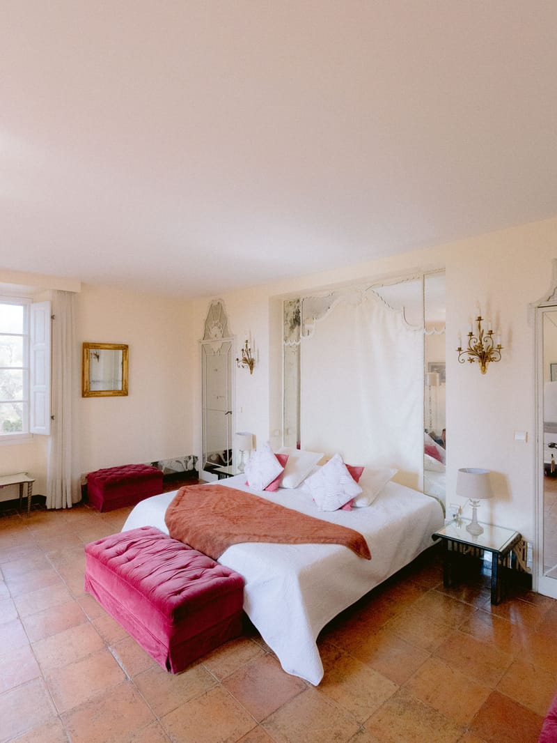 French chateau bedroom with white linens, raspberry pink velvet ottomans, and gold accents