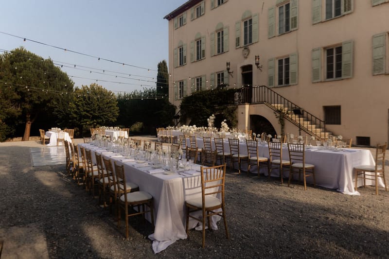Outdoor courtyard reception setup with gold chiavari chairs and white floral centerpieces at chateau