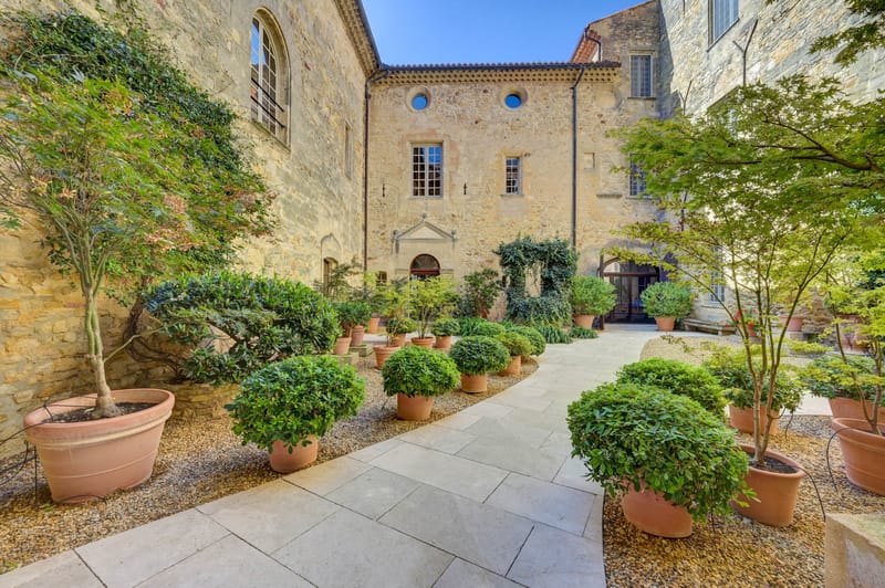 Limestone courtyard of a historic French chateau with arched windows and terracotta pots of clipped boxwood topiaries